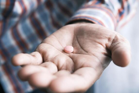A man holds a small, round, white pill in his open palm
